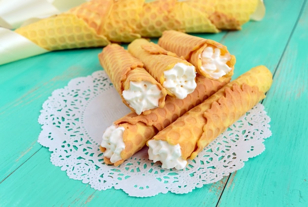 Tender honey wafers in the form of tubes, stuffed with air cream on white lace napkin. Close-up.