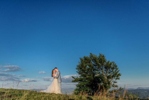 Tender hugs of wedding couple standing on the hill