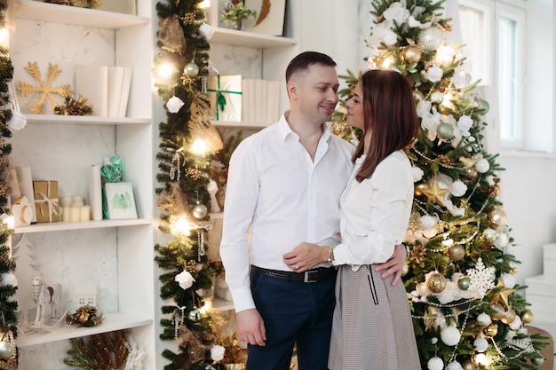 Tender husband and wife looking at each other while hugging in front of Christmas tree