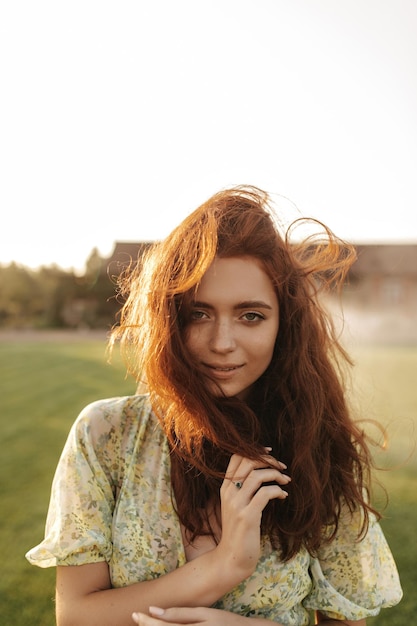 Tender lady with foxy long hairstyle and cute freckles in modern cool green dress smiling and looking into camera outdoor