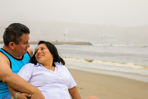 Tender older ethnic couple in love sitting on the sand on a beach