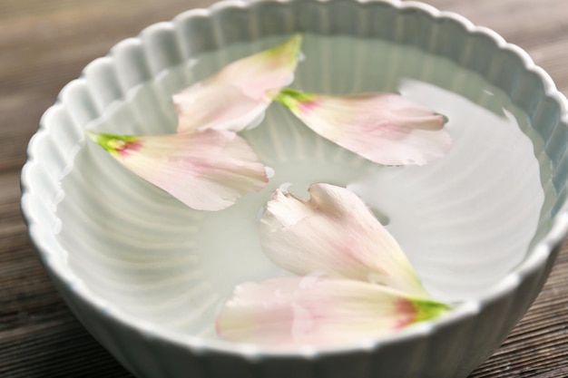 Tender pink rose petals in a bowl of water on wooden background