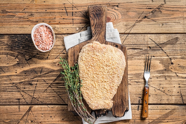 Tender Raw Breaded Wiener schnitzel on a wooden board with thyme. wooden background. Top view.