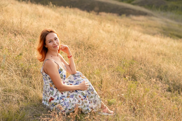 Tender red-haired woman enjoys the sunset in a field with a hill.