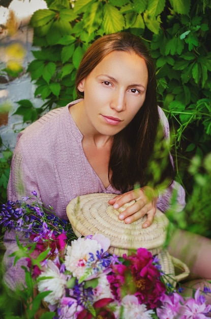 Нежная женщина отдыхает в травянистых зарослях с красивым букетом пионов и полевых цветов