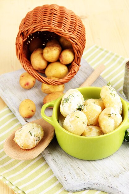 Tender young potatoes with sour cream and herbs in pan on wooden board on table closeup