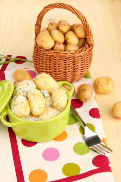 Tender young potatoes with sour cream and herbs in pan on wooden table closeup