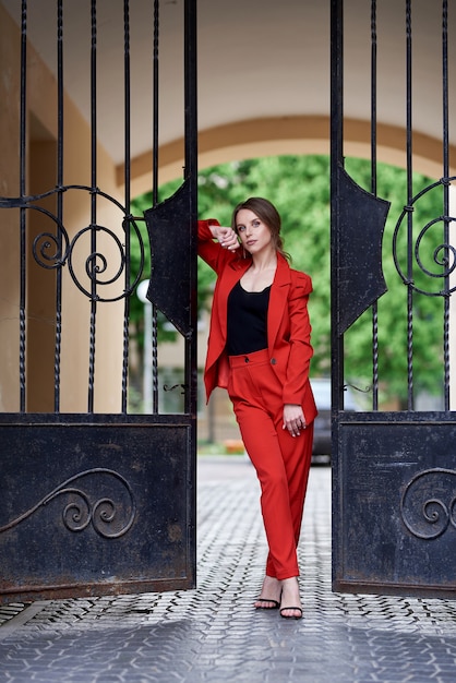 Tender young woman in the red suit, standing near the gates.