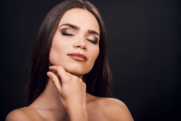 tenderness in each touch. beautiful young shirtless woman touching her face and keeping eyes closed 