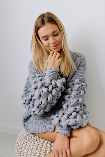 Foto la tenerezza bella donna con i capelli biondi in elegante pullover lavorato a maglia sta posando con un bel sorriso e gli occhi chiusi su sfondo isolato