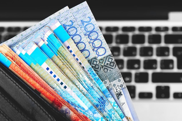Tenge. soldi di carta kazako in portafoglio nero sul primo piano del fondo del computer portatile.