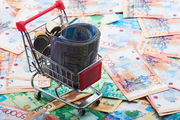 Tenge. A pack of Kazakh banknotes in a shopping cart on the background of a pile of money. Close up.