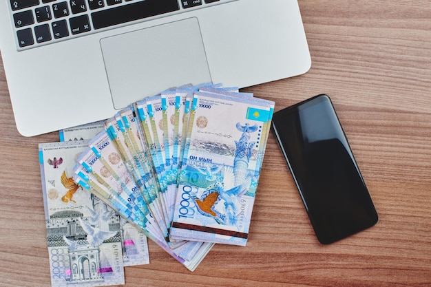 Tenge. Papier Kazachs geld, mobiele telefoon en computer op tafel close-up.