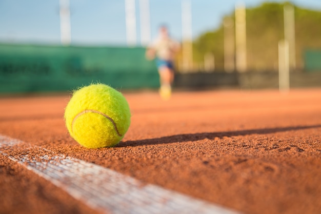 Tennis ball lying on white line on tennis court on sunny day.