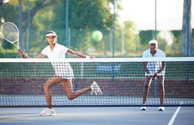 写真 テニスフィットネスと、サーブを返す競争ゲーム中にネット越しにボールを打つスポーツ女性女性アスリートとコートでプレーするダブルスのパートナーとの健康運動やトレーニング