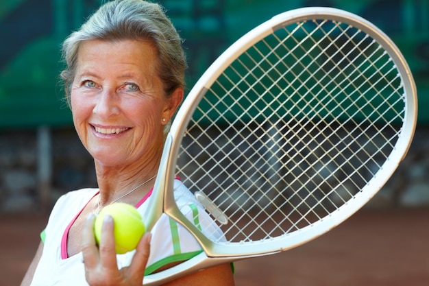 Tennis is her game Senior woman smiling while holding a tennis racquet and ball