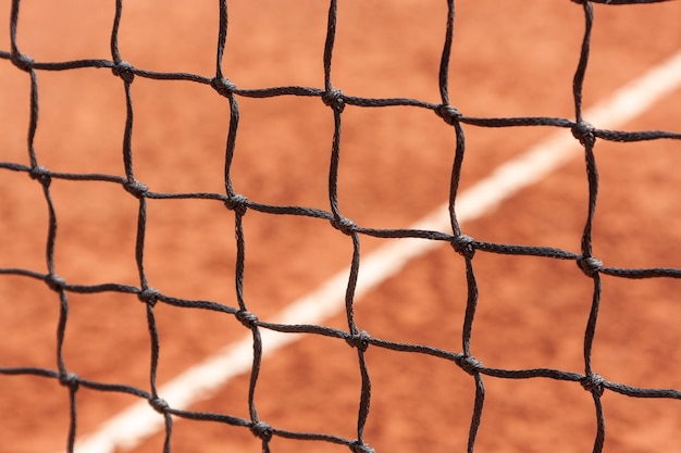 Foto rete da tennis vista ravvicinata dei nodi di una rete sportiva sullo sfondo di un campo con una superficie a terra