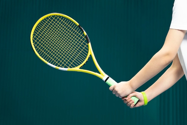 Tennis racket in hands of a girl close up on a dark green background the game of tennis