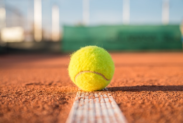 Tennisbal die op witte lijn op tennisbaan op zonnige dag liggen.