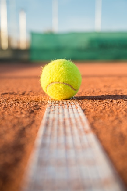 Tennisbal die op witte lijn op tennisbaan op zonnige dag liggen.