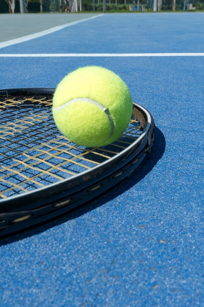 Tennisracket en bal op de blauwe vloer van de rechtbank. Harde verlichting. Selectieve aandacht.