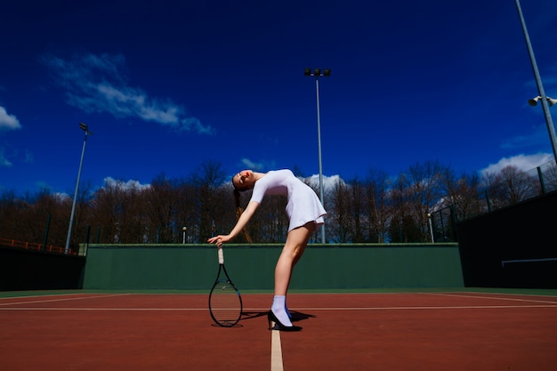 Tennisser in witte jurk en hakken met tennisracket op de rechter