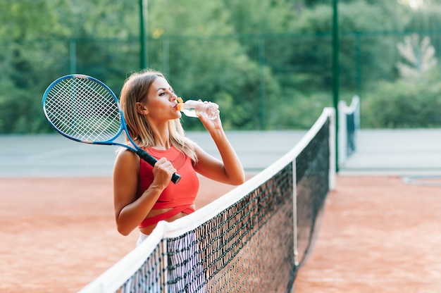 Tennisspeelster met handdoek op haar schouders drinkwater na wedstrijd