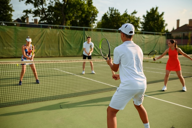 Tennistraining gemengd dubbel, buitenbaan. Actieve gezonde levensstijl, mensen spelen sportgame met racket en bal, fitnesstraining met rackets