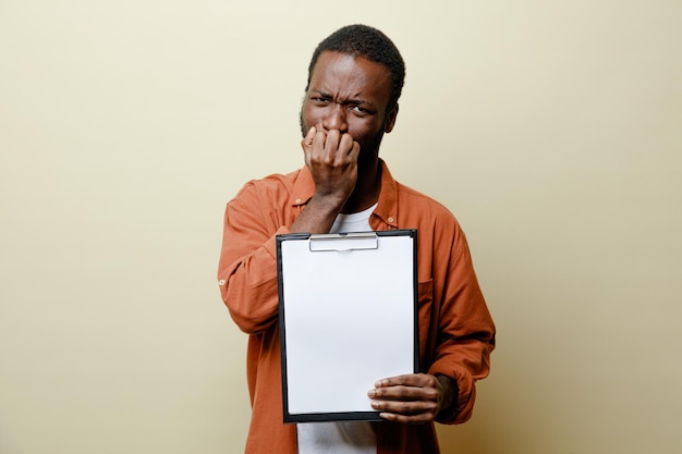 Tense grabbed chin young african american male holding clipboard isolated on white background