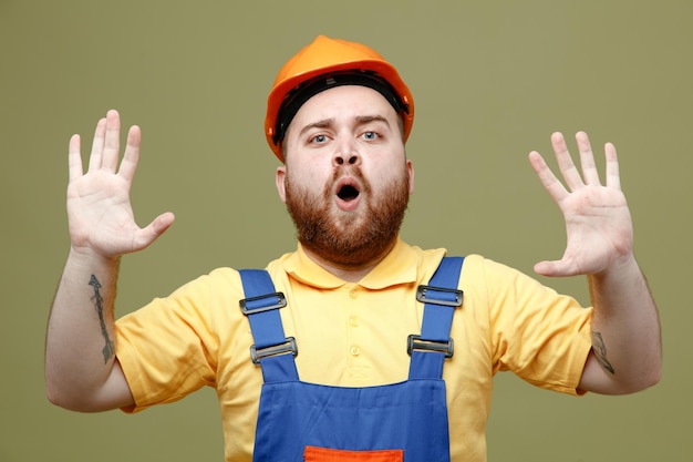 Tense spreading hands young builder man in uniform isolated on green background