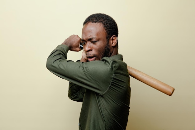 Tense young african american male wearing green shirt holding baseball bat isoloated on white background