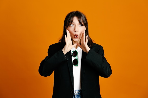 Tense young beautiful female wearing black jacket isolated on orange background