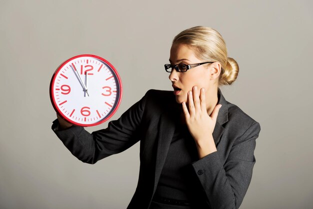 Photo tensed businesswoman holding clock against gray background