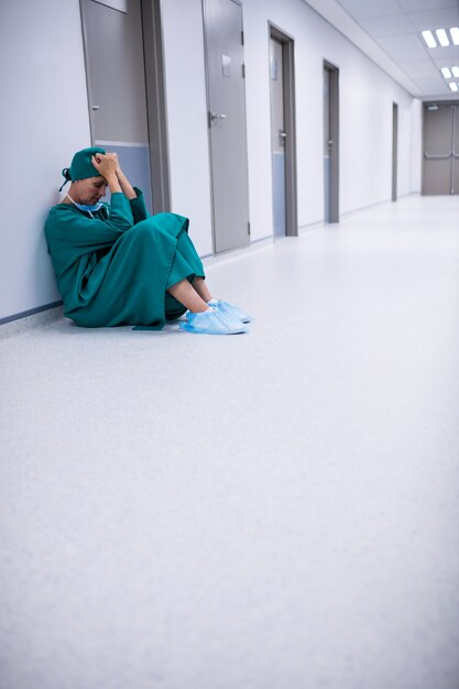 Tensed female surgeon sitting in corridor