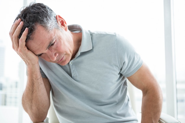 Tensed man sitting against window with his hand on head