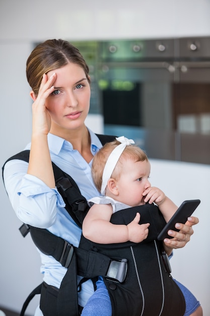 Tensed woman with mobile phone carrying baby girl