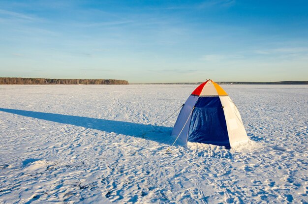 A tent with a fisherman in winter on the ice of the lake.