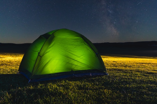 Tent with light on the countryside at night with stars