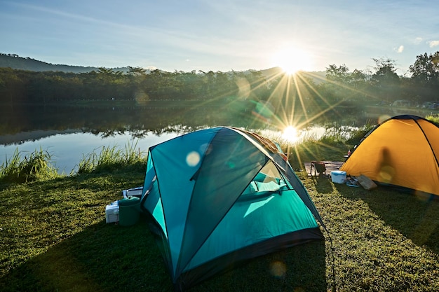 Tents on field by lake against bright sun