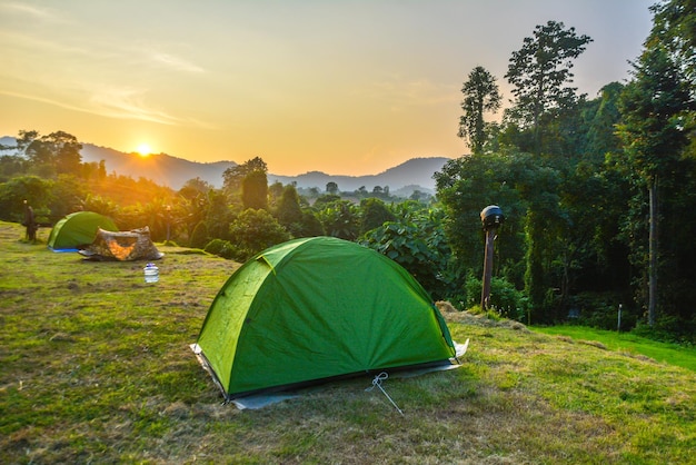 Tents on grassy mountain against sky during sunset