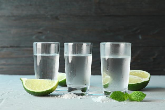 Tequila shots, salt, lime slices and mint on table against wooden