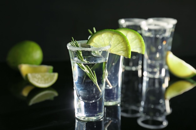 Tequila shots with juicy lime slices and salt on black background