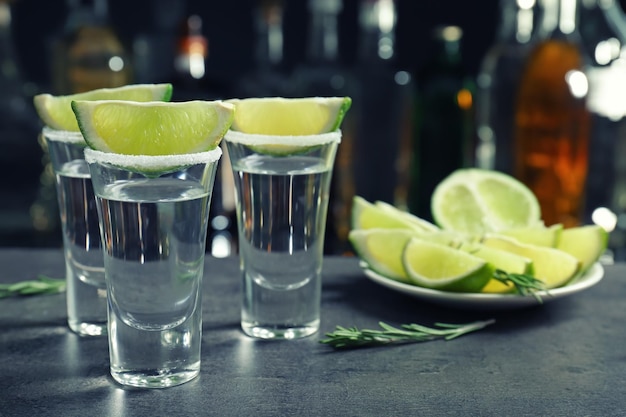 Tequila shots with juicy lime slices and salt on blurred background of glass bottles