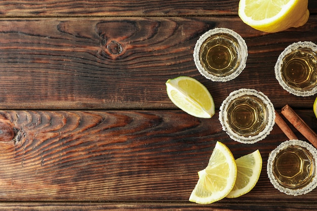 Tequila shots with salt, lime slices and cinnamon on wood table, top view