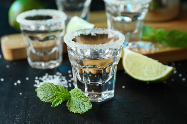 Tequila shots with salt, lime slices and mint on black table