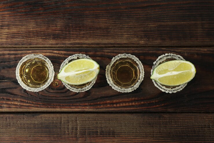 Photo tequila shots with salt and lime slices on wood table, top view
