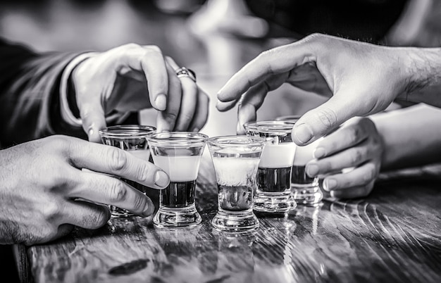 Tequila shots, wodka, whisky, rum. Cocktail in de nachtclub. Groep vrienden tequila shot glazen in bar. Mannelijke handen glazen shot of likeur. Zwart en wit.