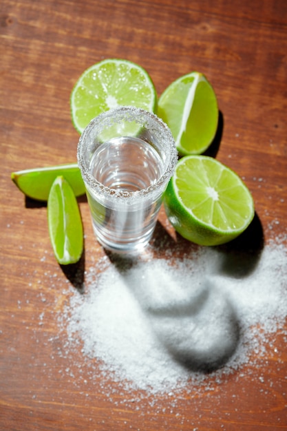 Tequila silver shots with lime slices and salt on wooden surface board