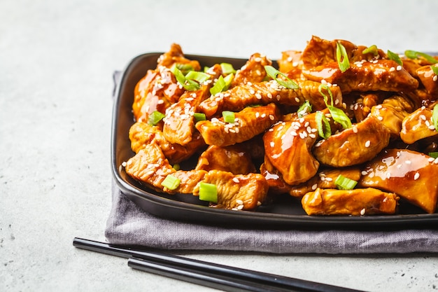 Teriyaki chicken with sesame, green onion in black plate.