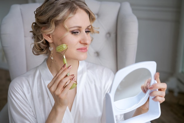 Term serene woman doing facial massage while sitting in chair in living room